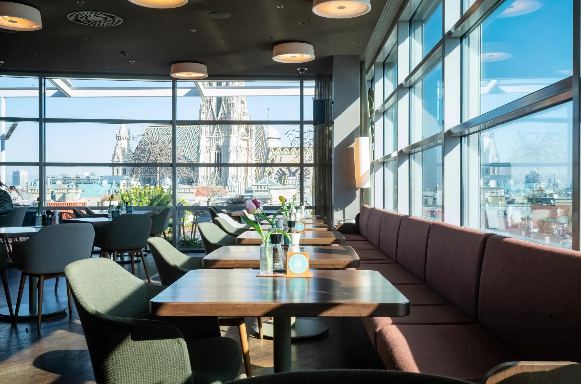 Modern restaurant with panoramic windows and a view of St. Stephen’s Cathedral in daylight