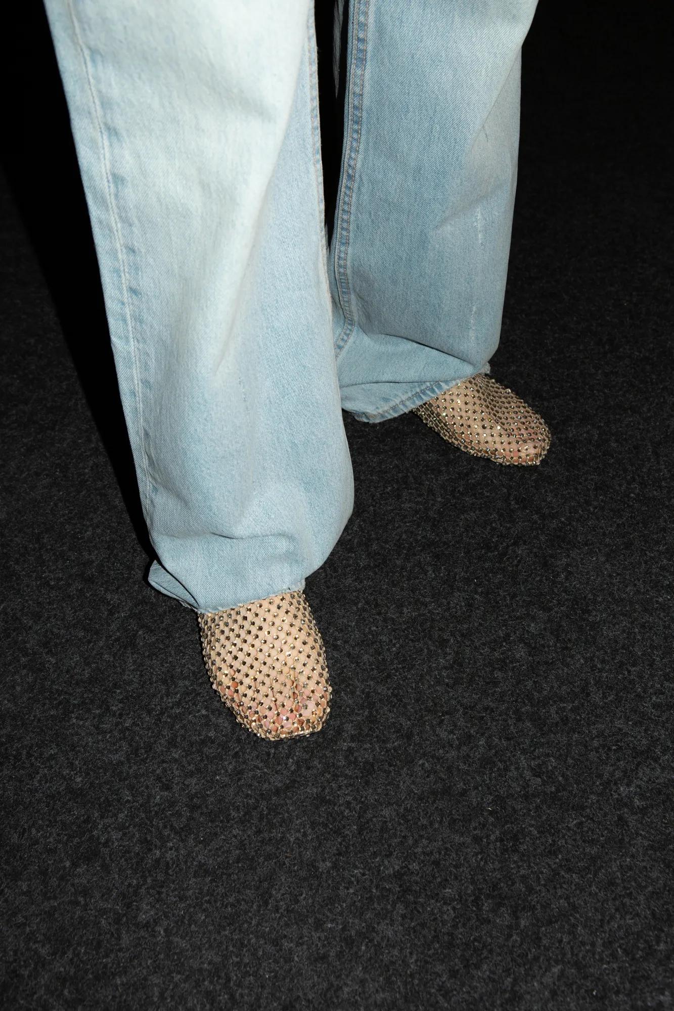 Light blue wide-leg jeans paired with sparkling mesh flats on a dark carpet