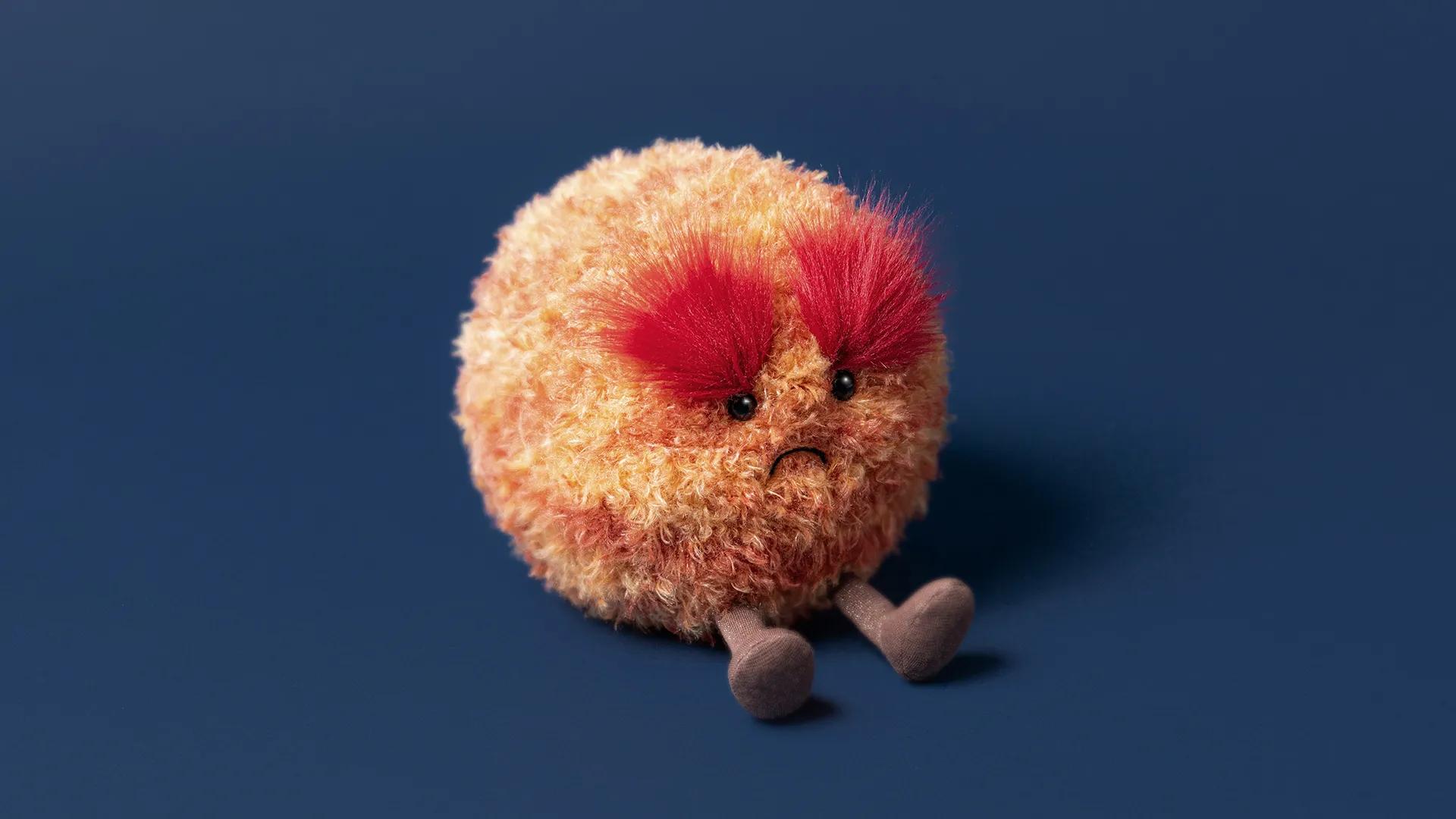 Fuzzy fantasy creature with bushy red eyebrows and a grumpy expression against a blue background