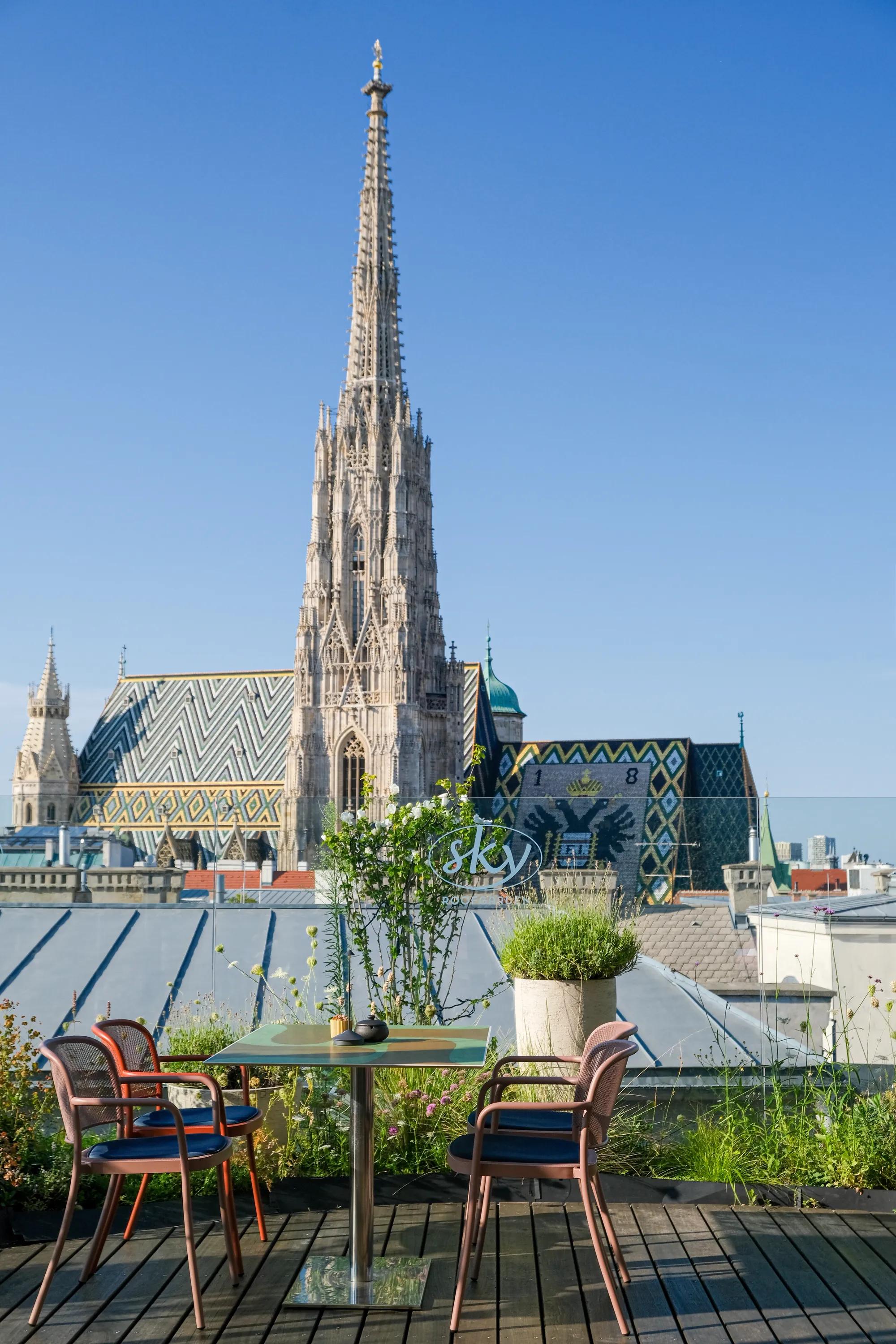 Rooftop terrace with seating area overlooking St. Stephen’s Cathedral in Vienna under a clear blue sky
