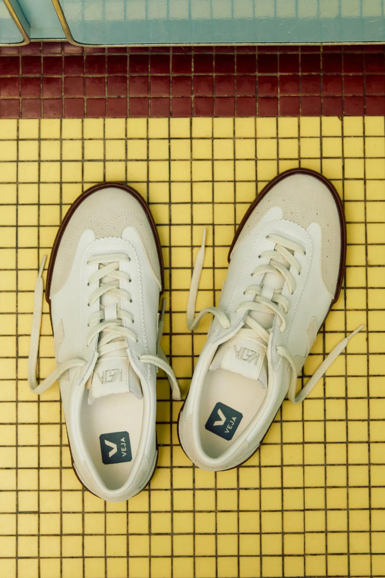 White sneakers with untied laces on a yellow tiled floor viewed from above