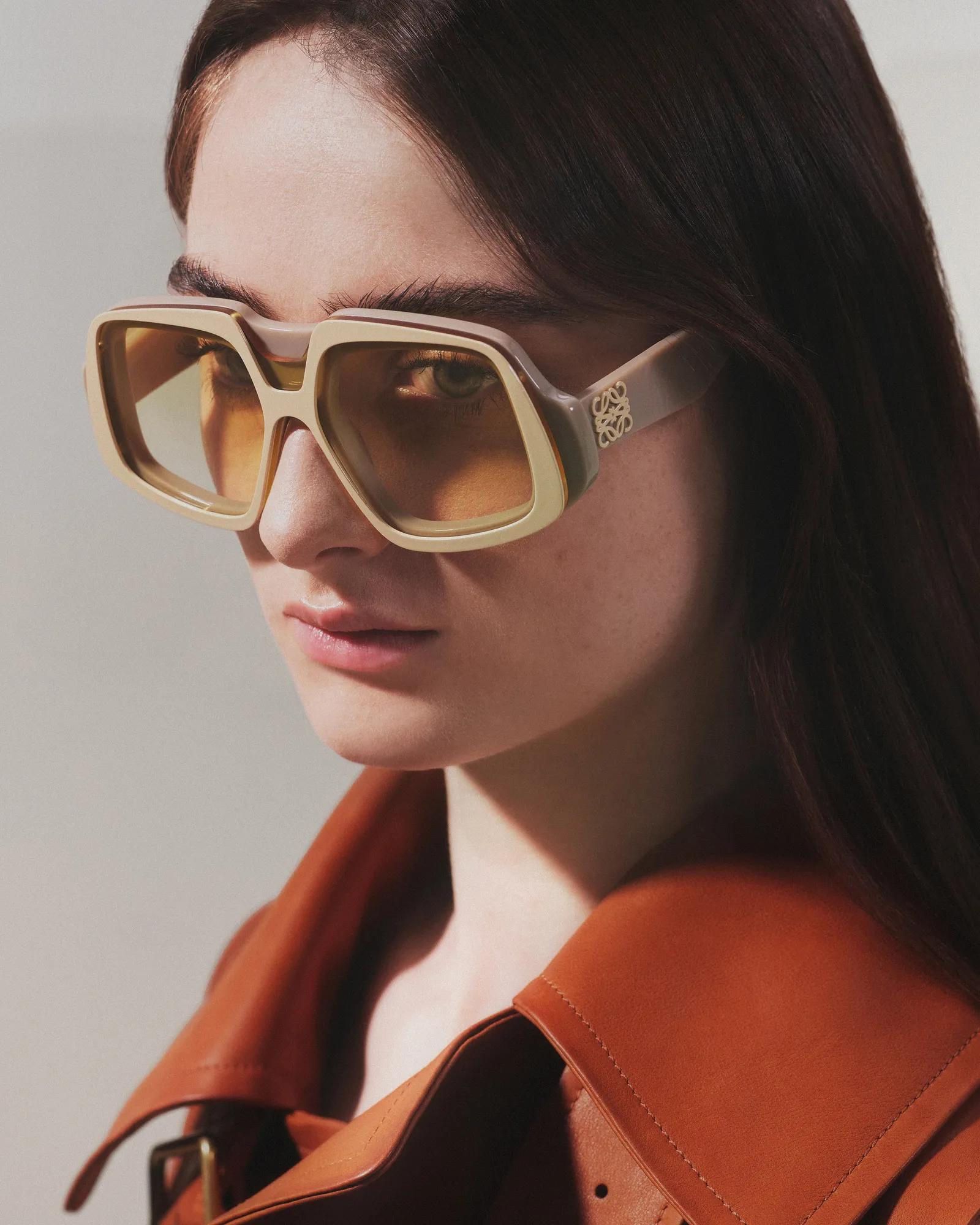 Close-up of a person wearing oversized square sunglasses and a brown leather jacket